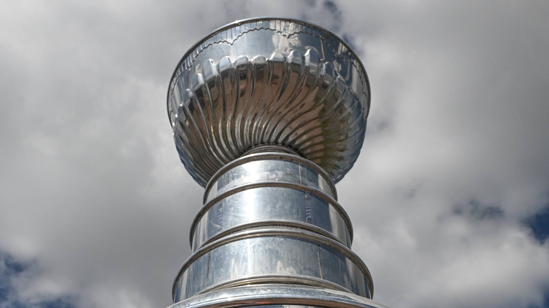 An Edmonton Oilers fan wearing a Connor McDavid jersey with the iconic number 97 stands in front of a giant replica of the Stanley Cup,