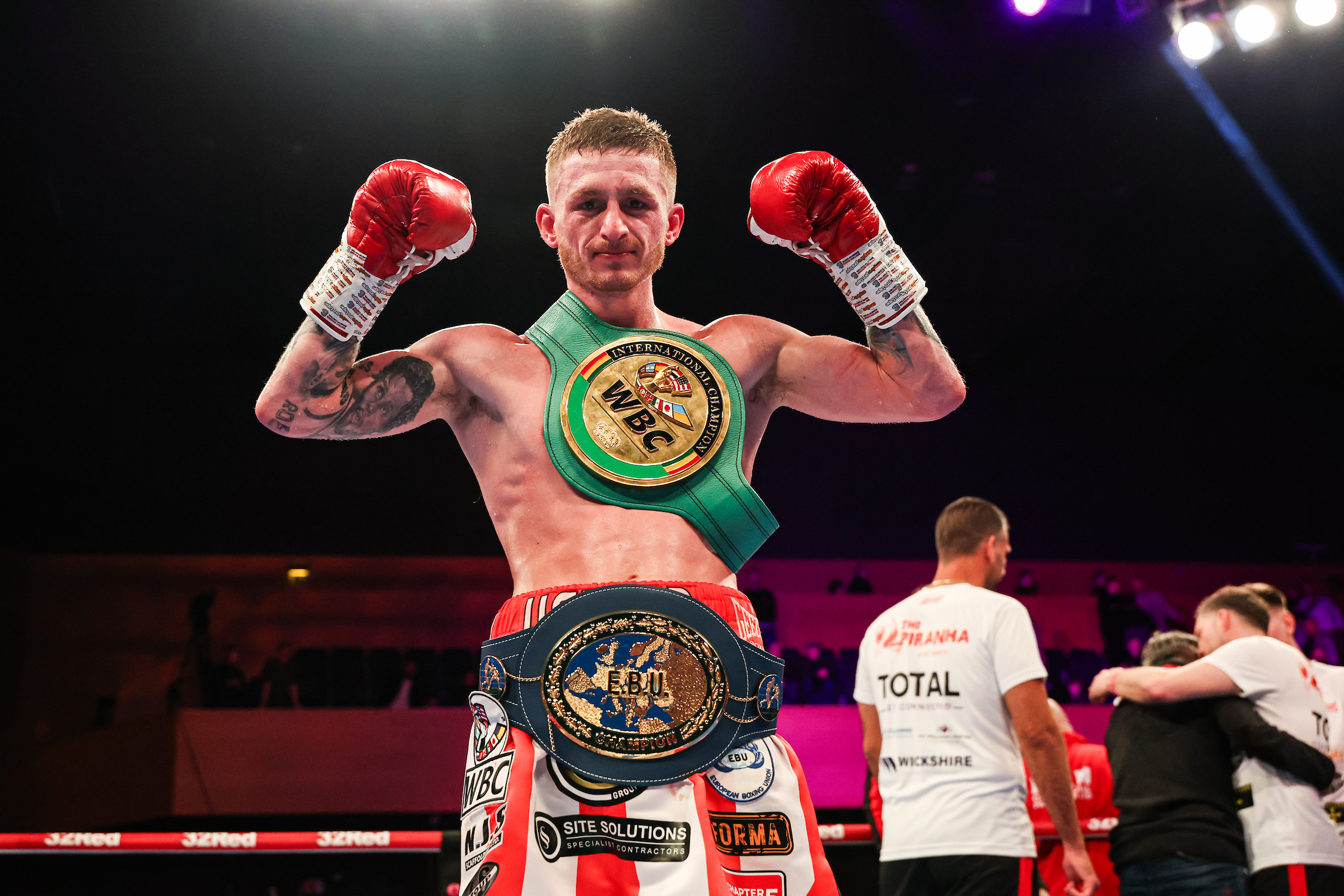 Ryan Garner stands arms aloft with the WBC silver and EBU super featherweight belts around his torso